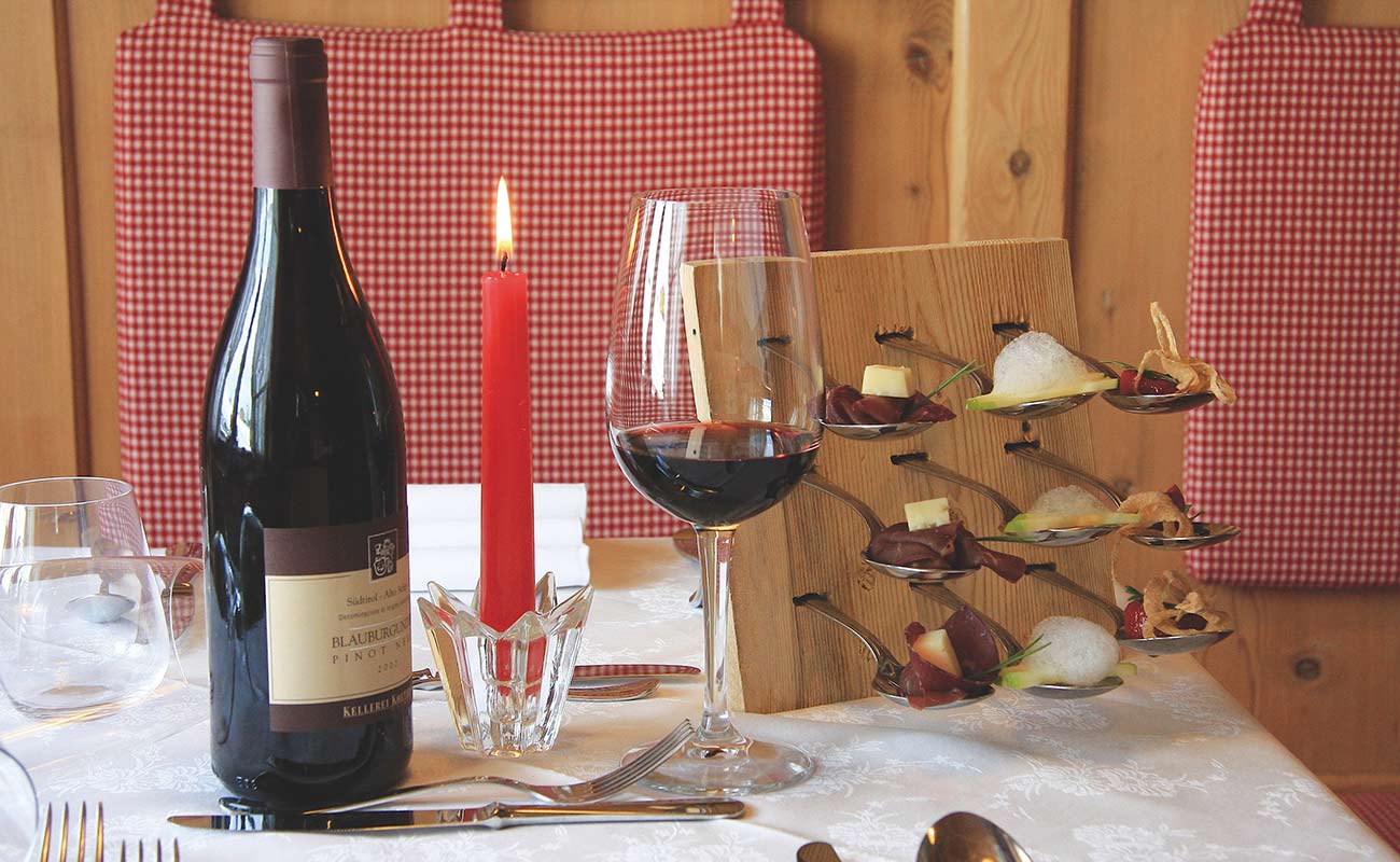 Burning red candle, bottle of red wine and filled red wine glass with finger food at the table